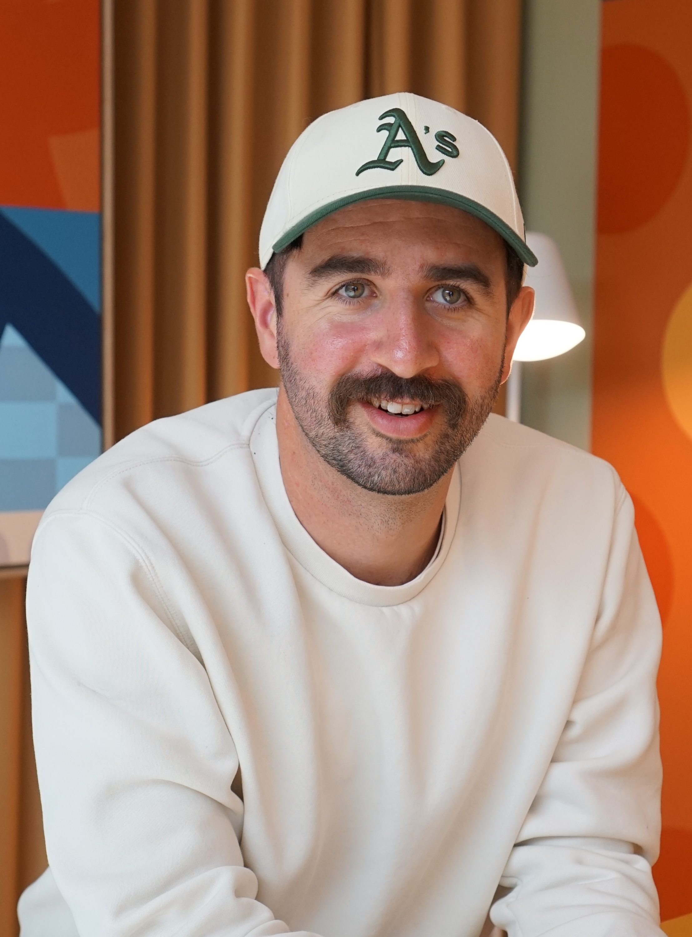 Eliot Prince smiling in a light sweatshirt and baseball cap