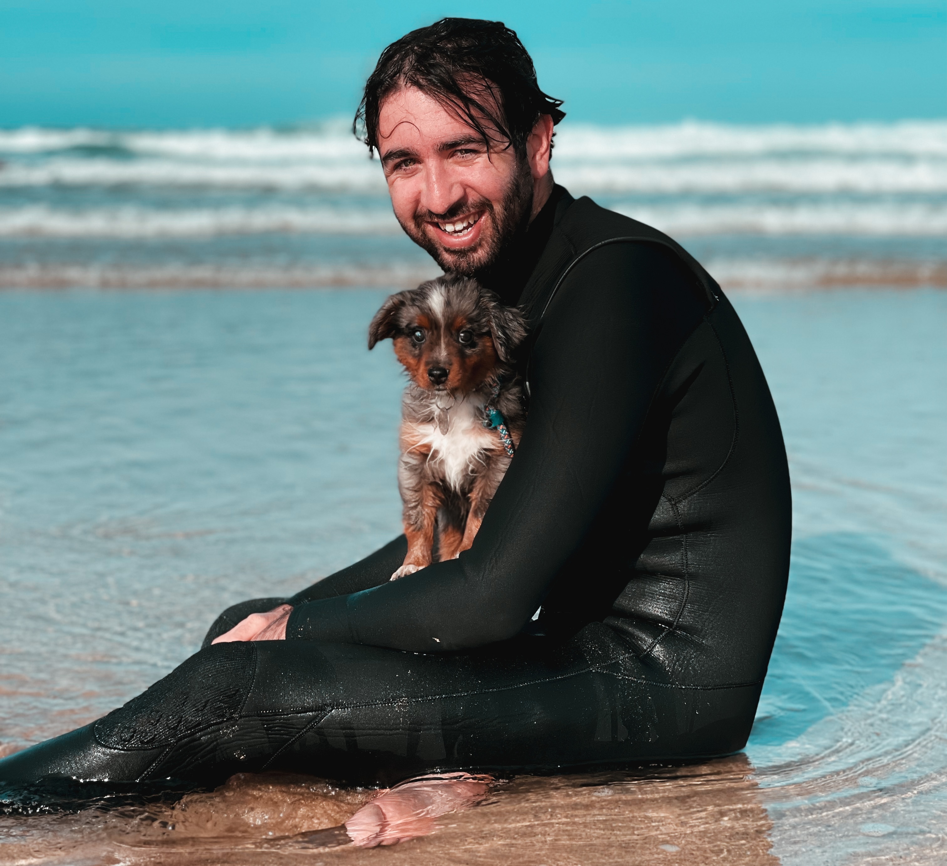 Eliot sitting in the sea with his dog on a beach